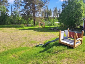 A grassy outdoor area with a wooden bench, a swing set, and a small wooden structure.