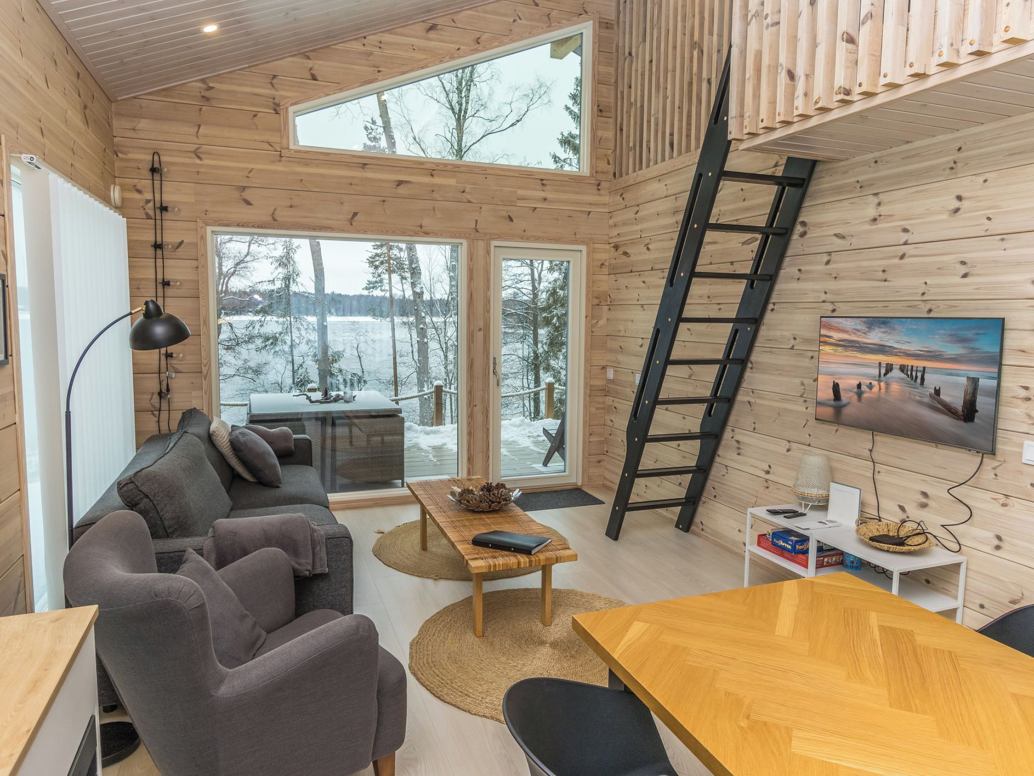 Ein gemütliches Blockhaus-Interieur mit einer Couch, einem Esstisch und einem großen Fenster mit Blick auf eine verschneite Landschaft.