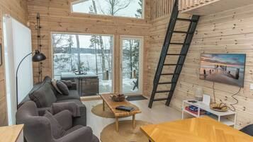 Ein gemütliches Blockhaus-Interieur mit einer Couch, einem Esstisch und einem großen Fenster mit Blick auf eine verschneite Landschaft.