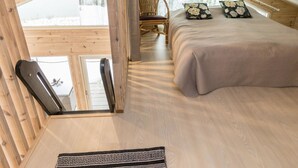 A cozy attic bedroom with a large bed, a wooden chair, and a view of the outdoors.