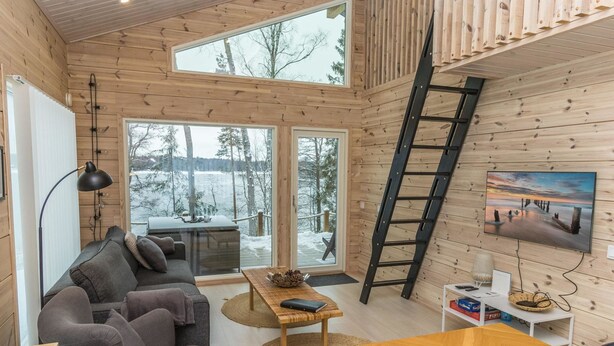 A cozy cabin interior with a sofa, a wooden table, and a TV mounted on the wall.