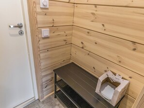 A corner of a room with wooden paneling, a door with a handle, a light switch, and a small bench with a box on it. - Villa korppi by Interhome (Kirkkonummi)