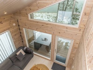A high-ceilinged wooden cabin with a sofa and a dining table, large windows, and a view of a snowy landscape. - Villa korppi by Interhome (Kirkkonummi)