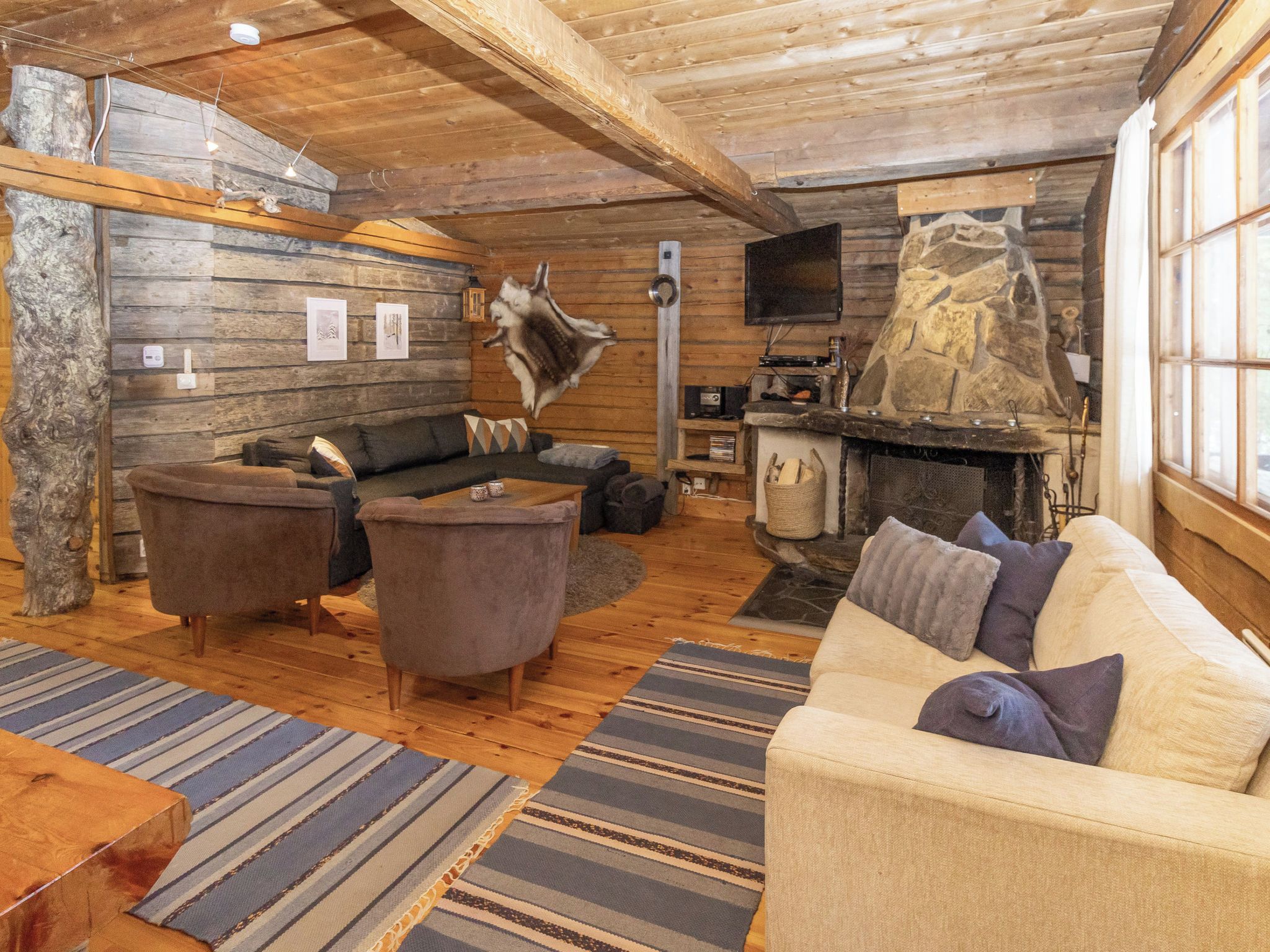 A cozy log cabin interior with a sofa, armchairs, a fireplace, and a stone wall.