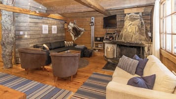 A cozy log cabin interior with a sofa, armchairs, a fireplace, and a stone wall.