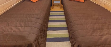 A cabin with two beds, each with an orange pillow, a small wooden table, and a striped rug.