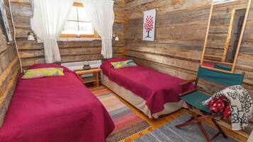 A cabin-style room with two beds, a bench, a mirror, and a window with curtains.