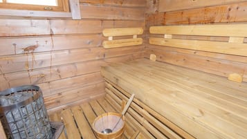 A sauna room with wooden benches, a stone-filled container, and a wooden bucket.