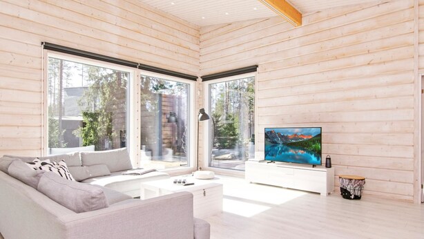 Een moderne woonkamer met een grote bank, een flatscreen televisie en grote ramen met uitzicht op de omgeving.