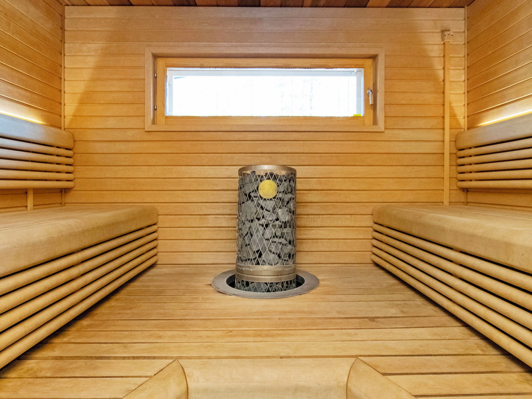 A sauna room with wooden benches, a central stone pillar, and a window.