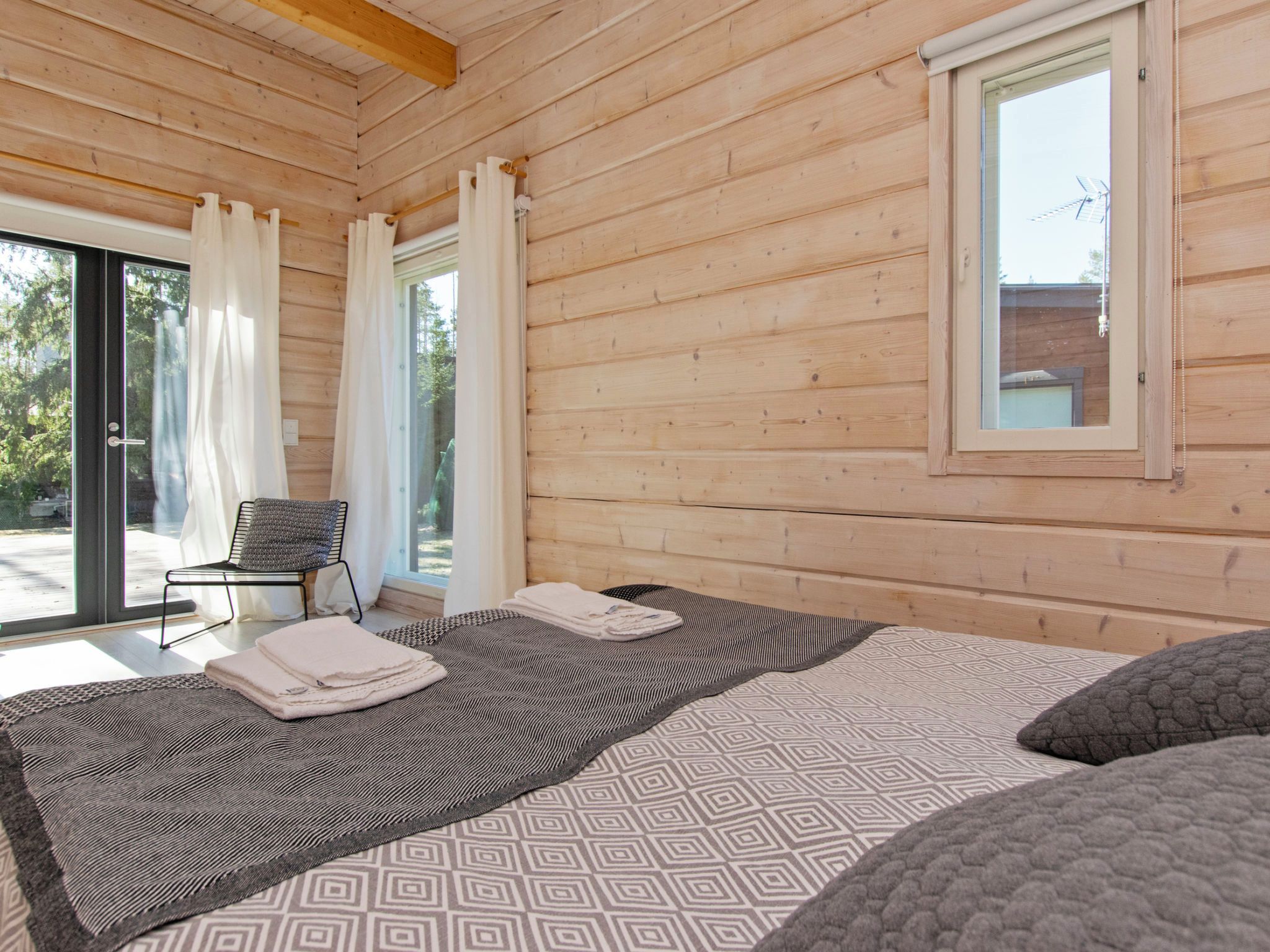 A wooden cabin room with a bed, a chair, and a window.
