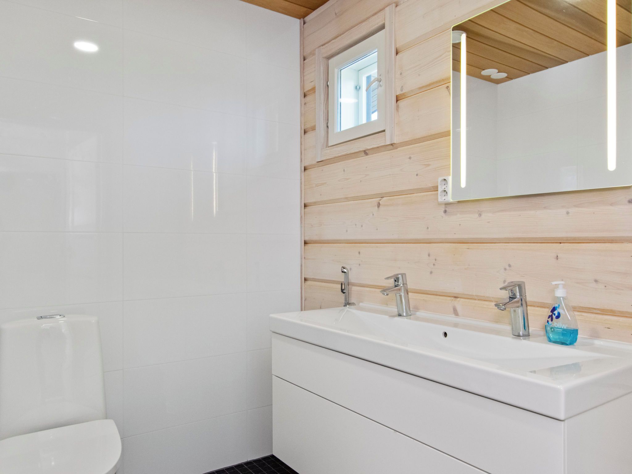 Un baño moderno con un lavamanos blanco, dos grifos, un espejo y un ventanal.