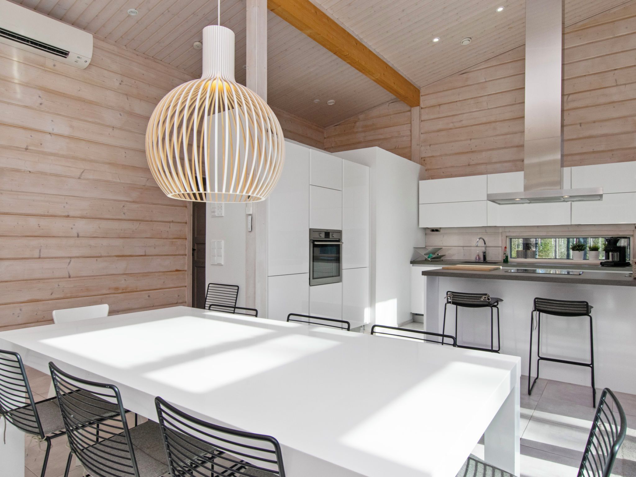 Una cocina moderna con armarios blancos, una campana extractora de acero inoxidable y una zona de bar con taburetes.