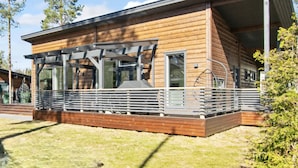Een moderne houten blokhut met een overdekt terras, grote ramen en een terras.