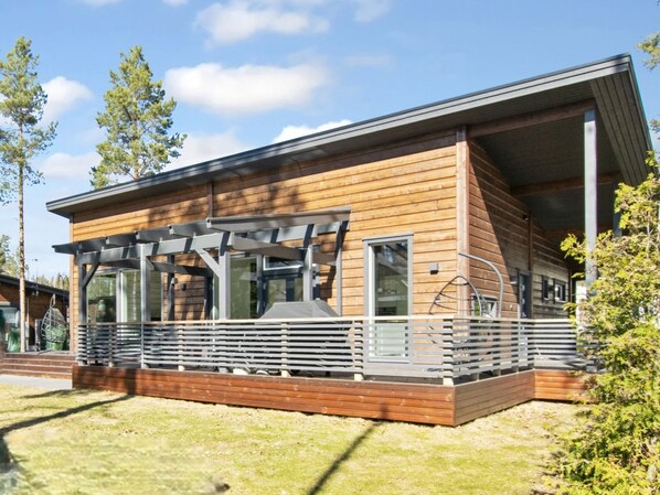A modern wooden cabin with a covered patio, large windows, and a deck.