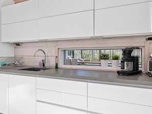 Una cocina moderna con armarios blancos, un lavamanos de acero inoxidable y una máquina de café.