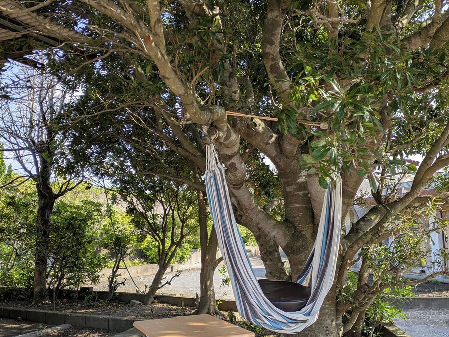 A hammock suspended from a tree, a foldable chair, and a gravel area.