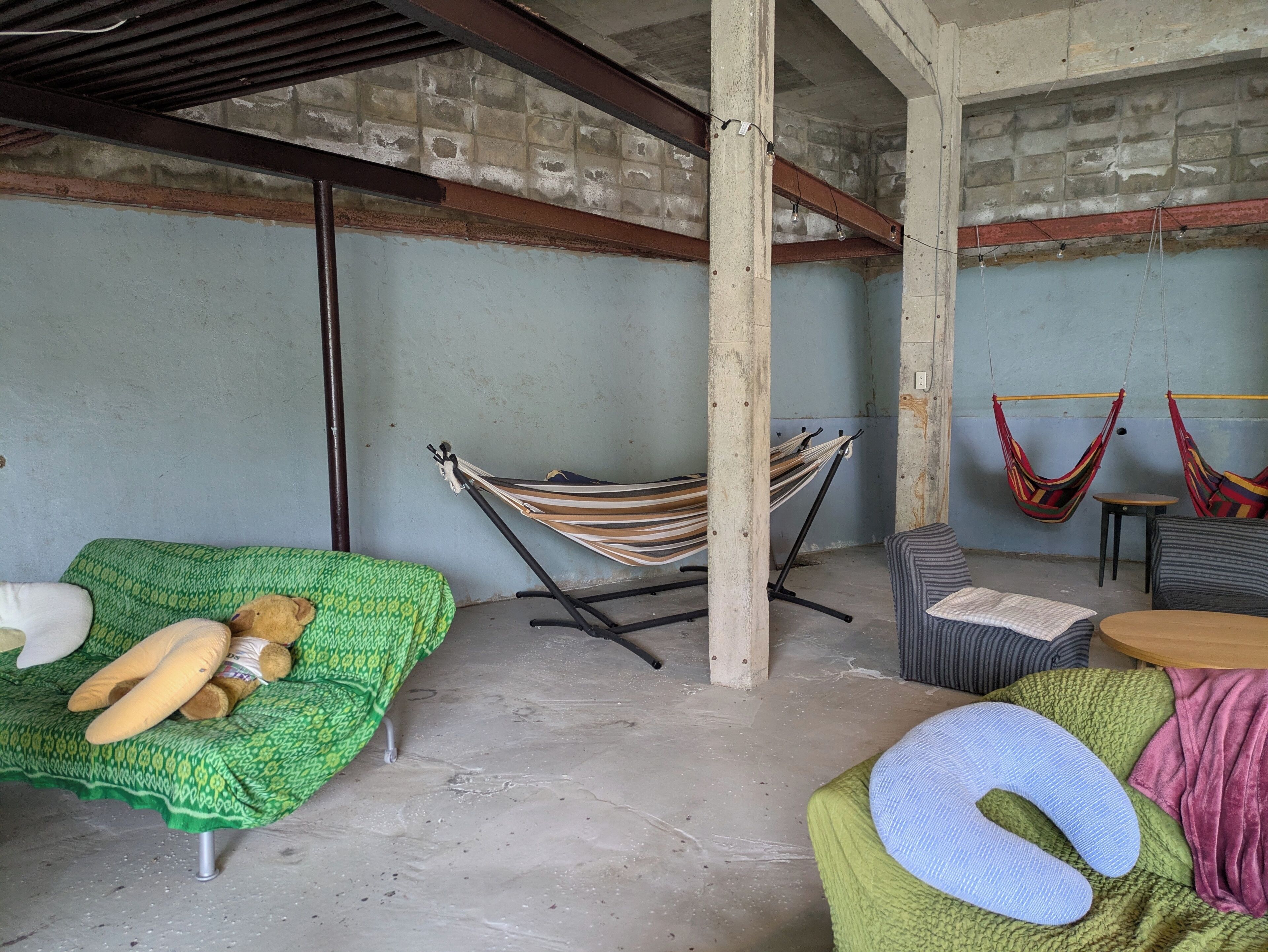 Una habitación con una hamaca, un sofá verde con un oso de peluche y una silla a rayas.