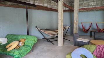 Una habitación con una hamaca, un sofá verde con un oso de peluche y una silla a rayas.