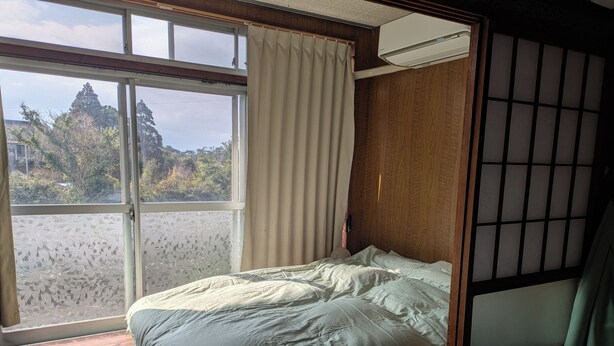 A room with a bed, a window with curtains, a view of trees, and a wooden partition.