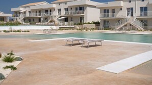 Un resort con piscina, tumbonas y un edificio de varios pisos con balcones.