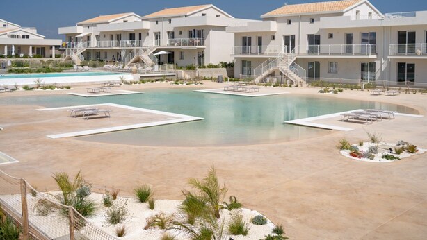 Un resort con varias edificaciones, una piscina central y zonas de estar al aire libre.