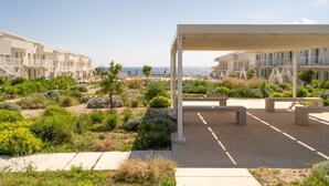 Un hotel moderno con varios balcones, una zona de estar al aire libre techada y un jardín ajardinado con diversas plantas.