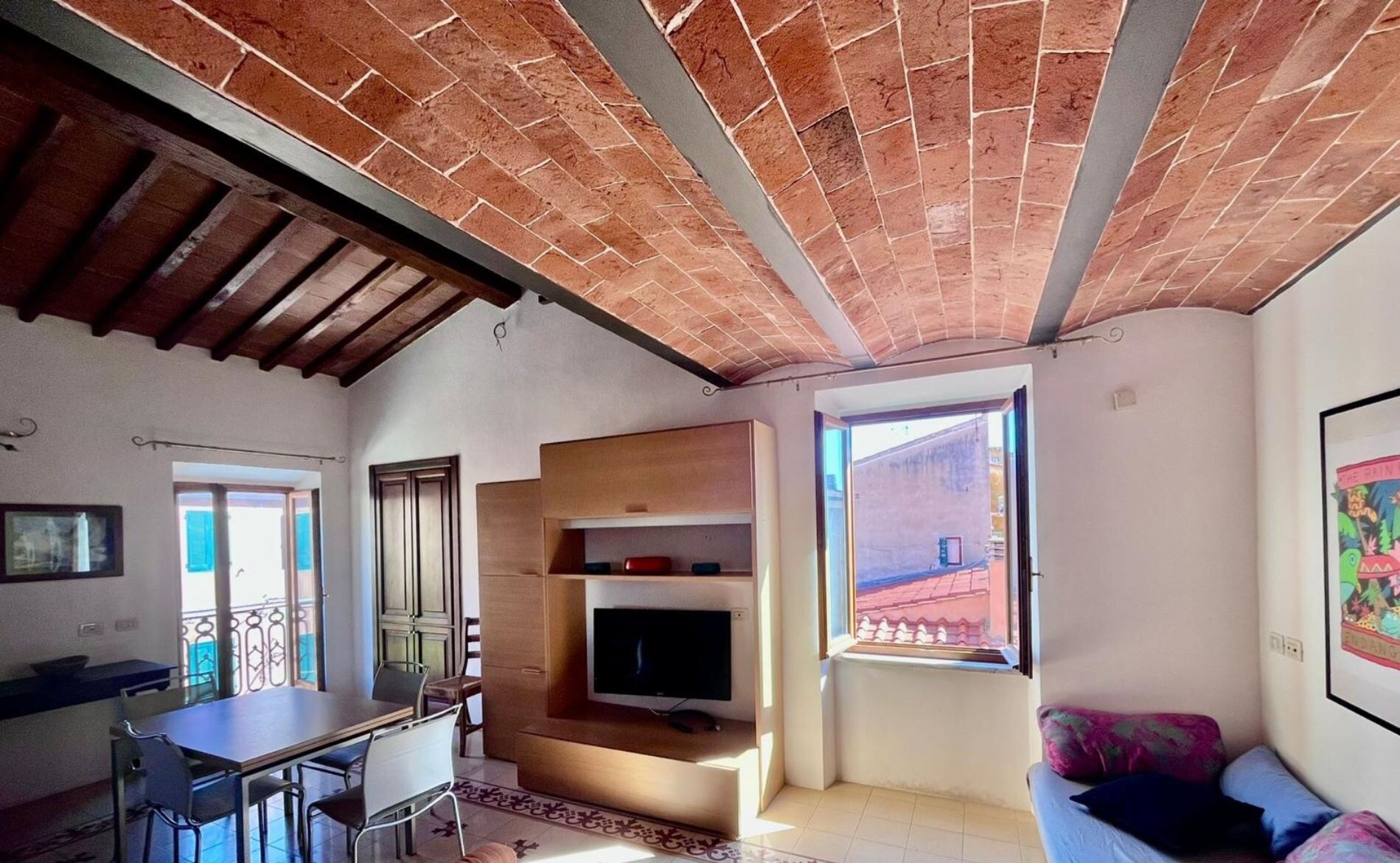 Una sala de estar con televisor, comedor con sillas, sofá y ventana con vistas.