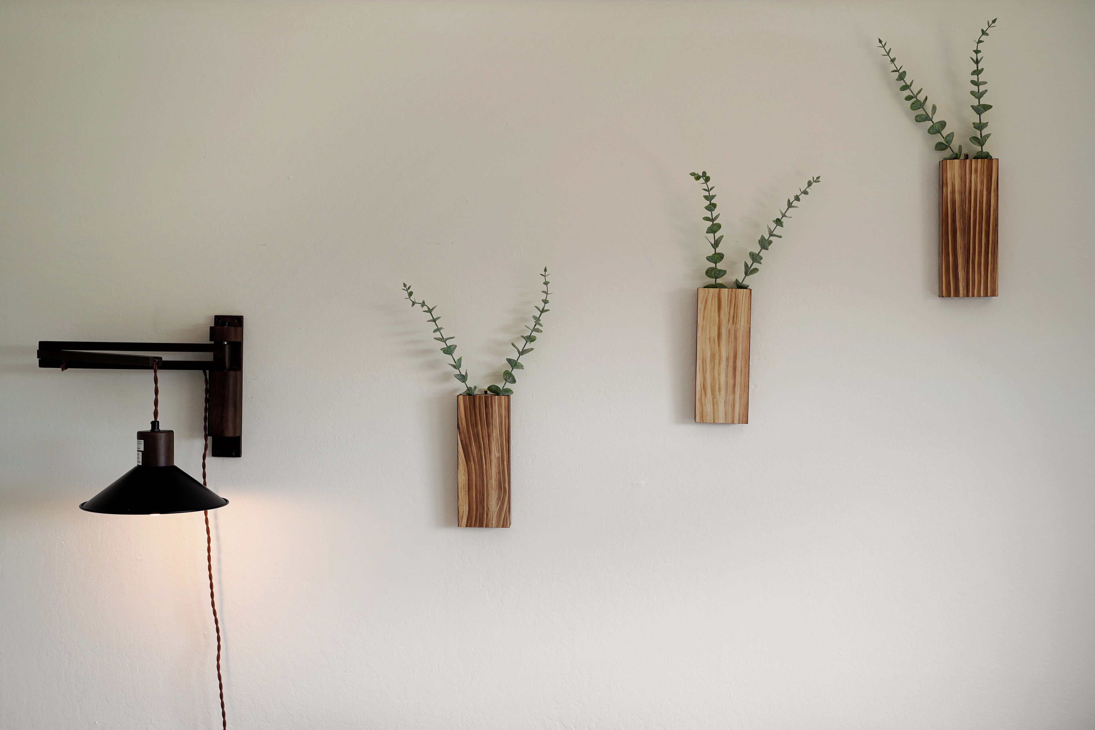 A wall-mounted pendant light and three wooden planters with green foliage.