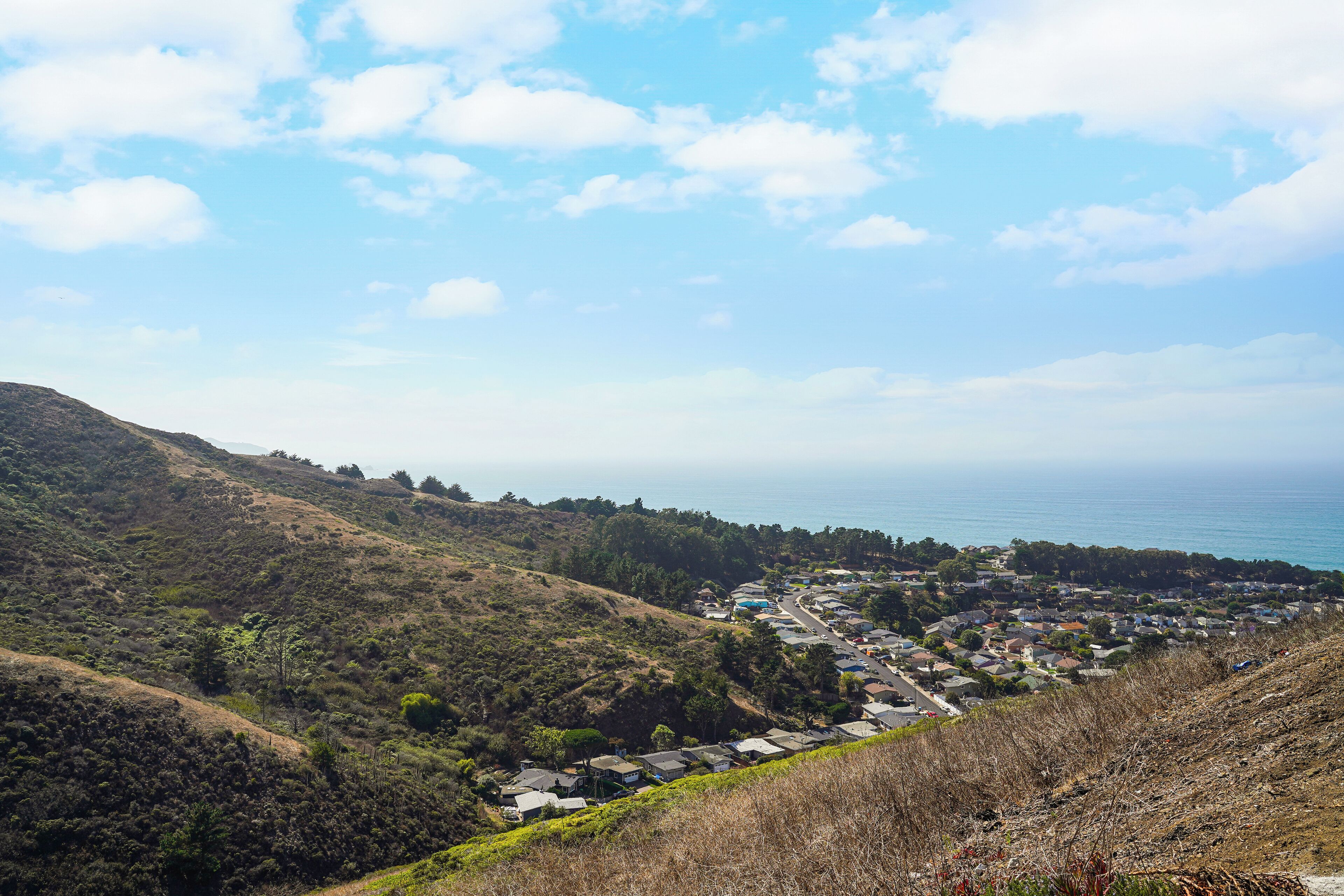 A coastal town with houses on a hillside, a clear sky, and the ocean in the background.