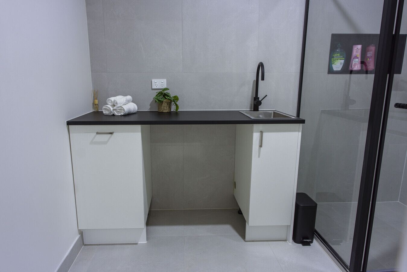 A compact bathroom with a sink, two cabinets, a towel rack, and a small potted plant.