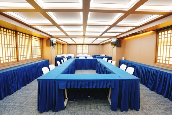 A conference room with a long table, white chairs, and a blue tablecloth.