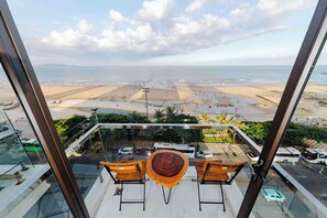A balcony with a view of a beach and a cityscape. There are two wooden chairs and a round table. - SIN OAE HOTEL (Ho Chi Minh City)
