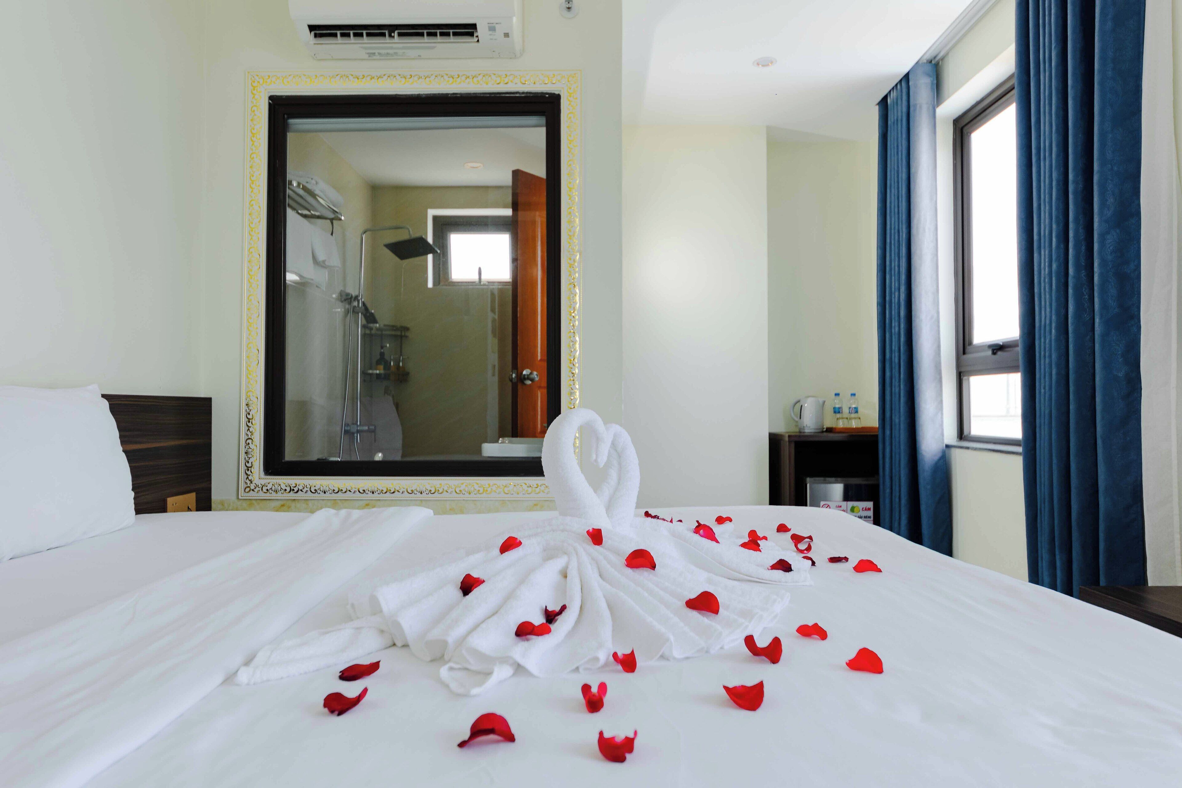 A hotel room with a large bed, a mirror, a shower, and a window with curtains.