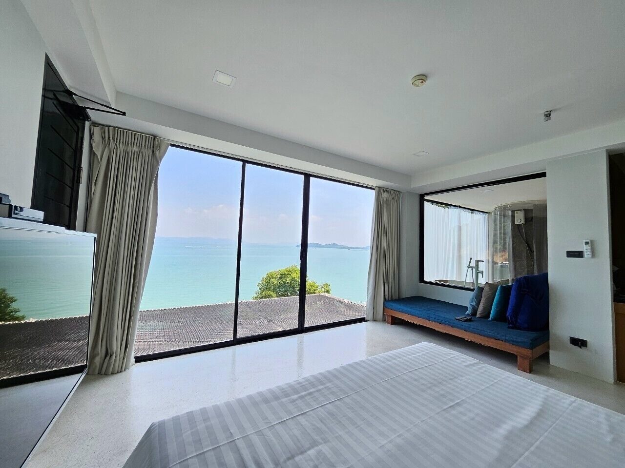 Un dormitorio moderno con una cama grande, un sofá junto a la ventana y vistas al mar.
