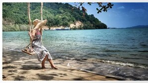 Une personne est assise sur une balançoire au-dessus d’une étendue d’eau, avec une colline boisée en arrière-plan.