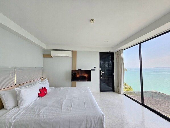 Une chambre d’hôtel moderne dotée d’un grand lit, d’un téléviseur à écran plat fixé au mur et d’un balcon offrant une vue sur la mer.