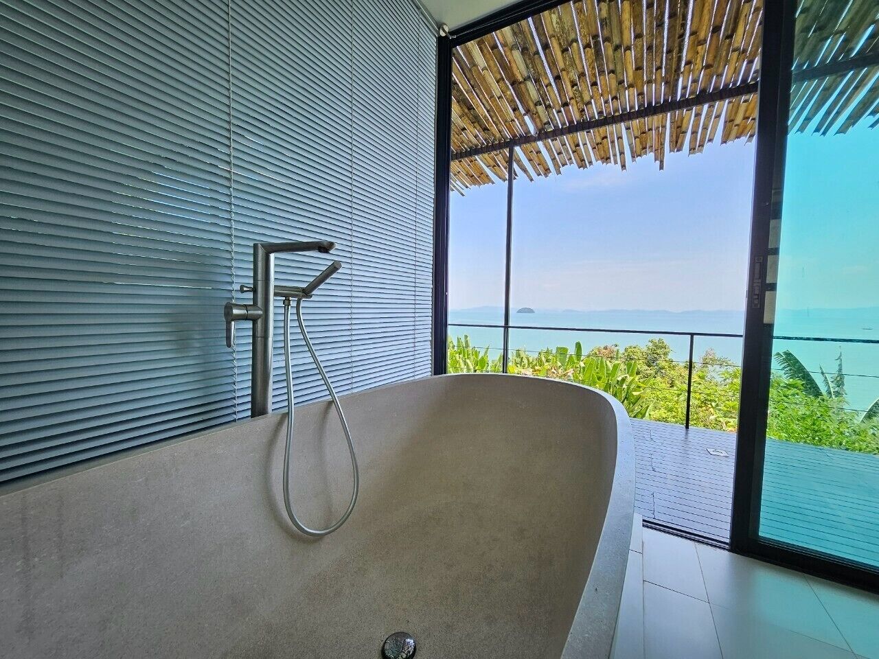 A modern bathroom with a freestanding bathtub, a shower, and a large window offering a view of the ocean.