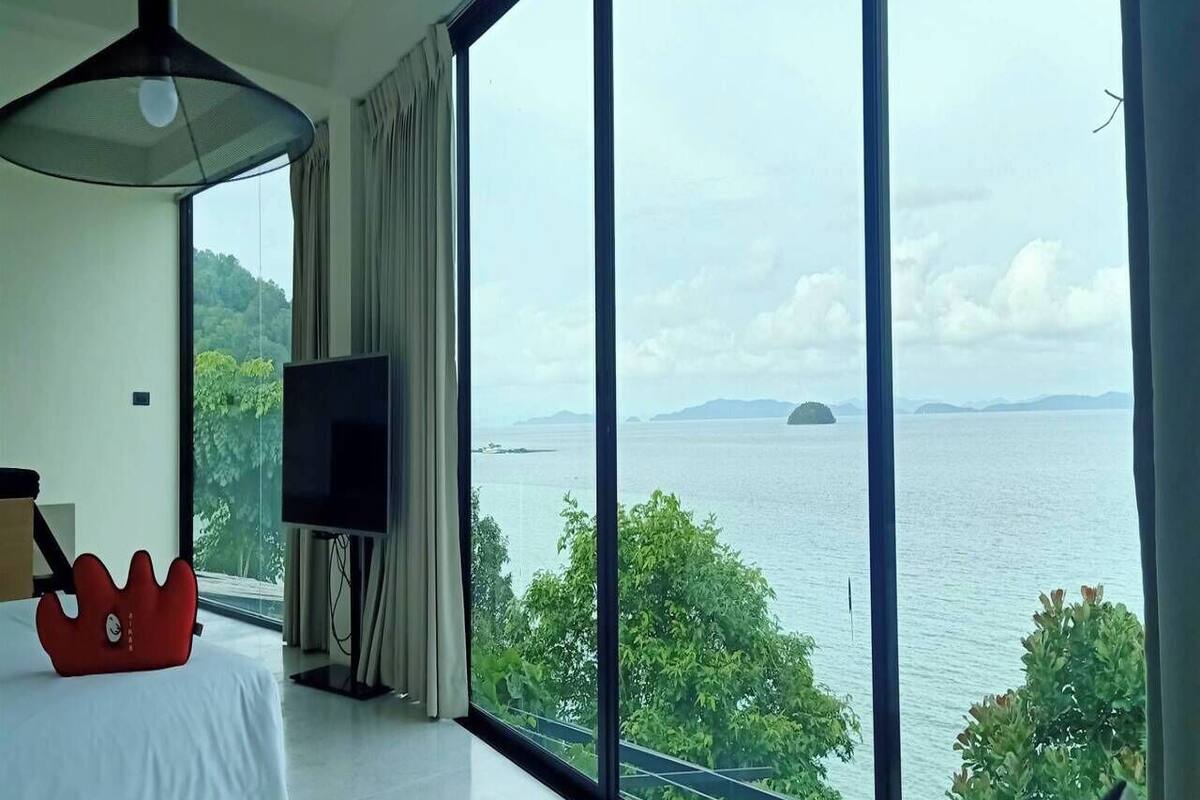 A bedroom with a large window overlooking a body of water and greenery.