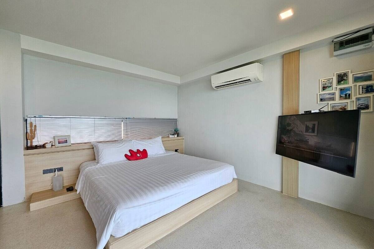 A modern bedroom with a bed, bedside tables, an air conditioning unit, a flat-screen TV, and a wall-mounted picture gallery.