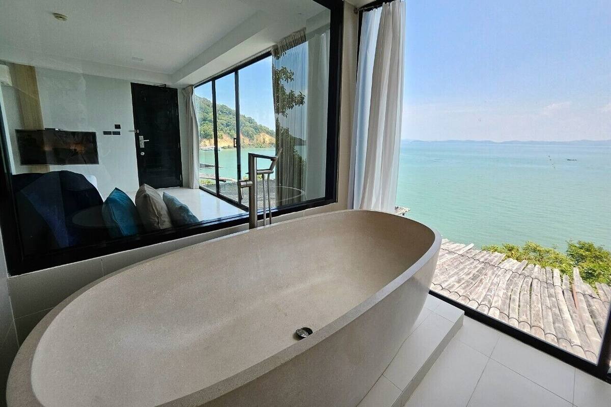 A modern bathroom with a freestanding bathtub, large windows, and a view of the sea.