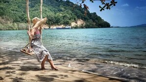 A person on a swing over a body of water with a forested hill in the background. - 8IK88 Resort (Pa Klok)