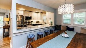 A modern kitchen with white cabinets, stainless steel appliances, and a marble island with bar stools. - Ocean Shade | Edisto Beach Vacation Rental | Private Pool Oasis | Walk to Beach (Edisto Beach)