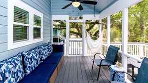 A covered porch with a blue and white color scheme, featuring a seating area with blue patterned cushions, a ceiling fan, and a hammock. - Ocean Shade | Edisto Beach Vacation Rental | Private Pool Oasis | Walk to Beach (Edisto Beach)