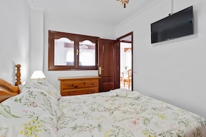 Un dormitorio con cama, cómoda de madera, televisor y ventana con cortinas.