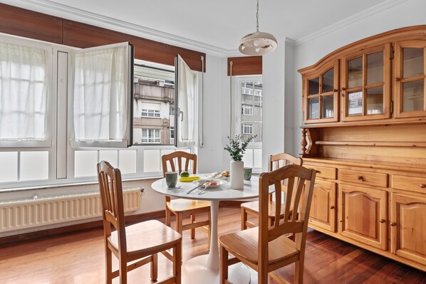 Un comedor con una mesa redonda, sillas de madera, una alacena con puertas de vidrio y una ventana con cortinas.