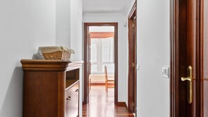 Een gang met een houten kast, een rieten mand en een deur naar een kamer met een radiator.