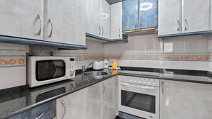 Een keuken met witte kastjes, een magnetron, een broodrooster en een oven.