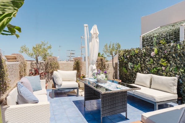 Una terraza en la azotea con mobiliario exterior, una mesa de vidrio y un muro decorativo.