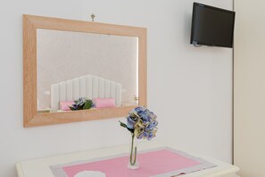 Una habitación con espejo, televisor, un jarrón con flores y un camino de mesa rosa.